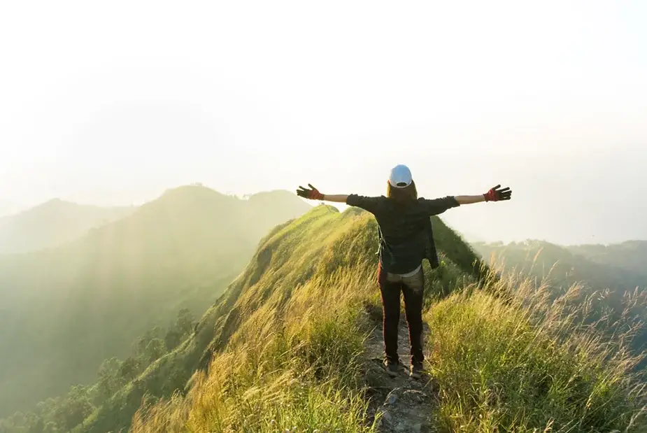 Client standing on mountain trail with open arms, celebrating freedom and successful property journey.