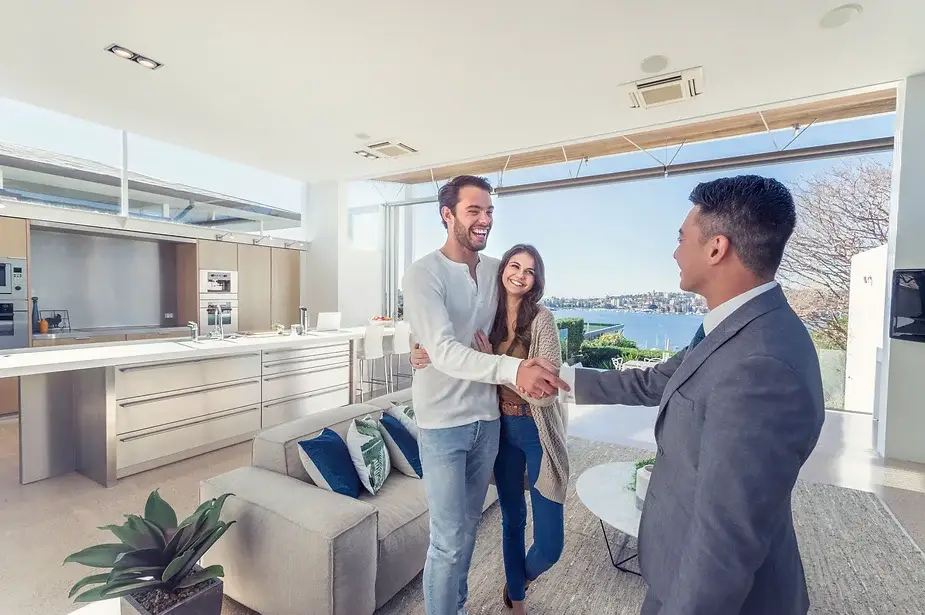 Happy couple shaking hands with a real estate agent in a modern Australian home with a scenic view.