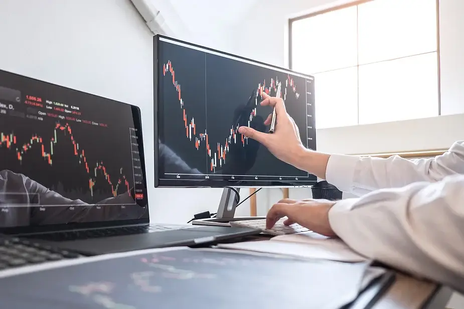 Investor analyzing stock market trends on multiple monitors, representing a comparison of property and stock investments.