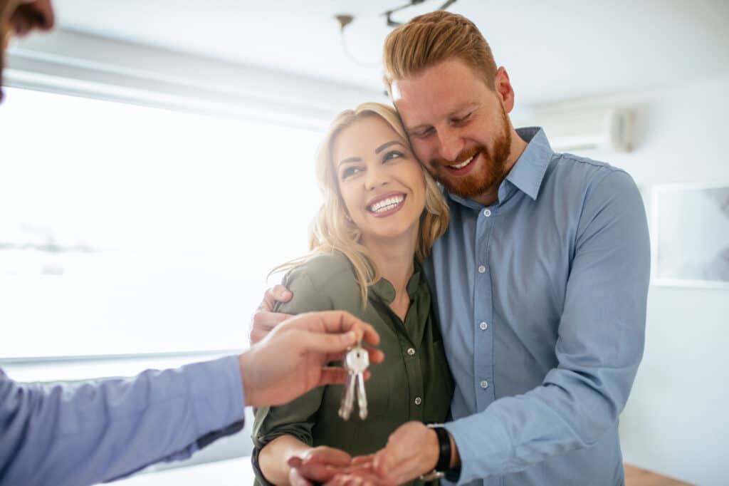 A smiling couple shaking hands with a professional buyer's agent after successfully purchasing a property